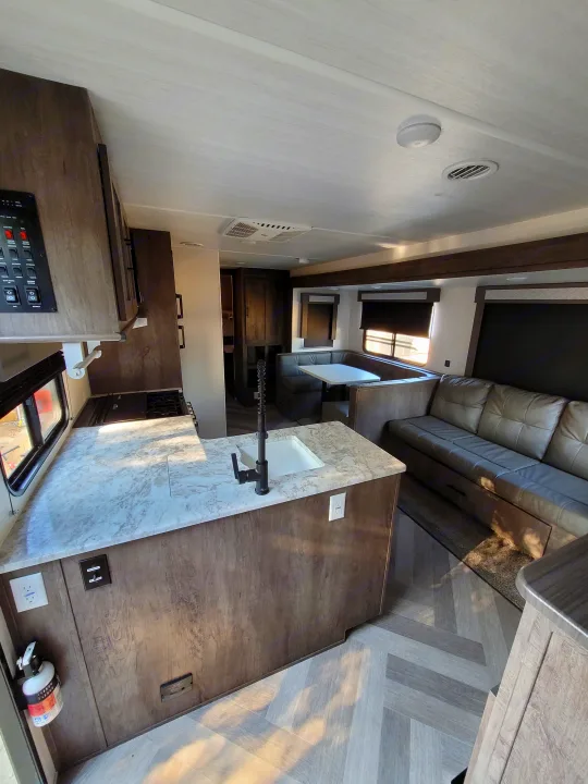 Inside a modern RV rental, showing the kitchen counter, sink, and living area with a comfortable couch and wood-look flooring.. Forest River Salem 2021