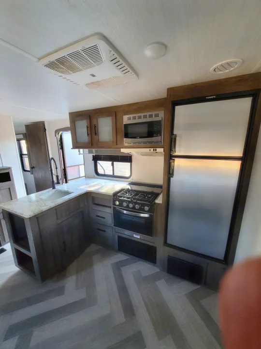 RV rental kitchen featuring a Dometic fridge, microwave, stove, oven, sink, and herringbone floor. Perfect for travel!. Forest River Salem 2021