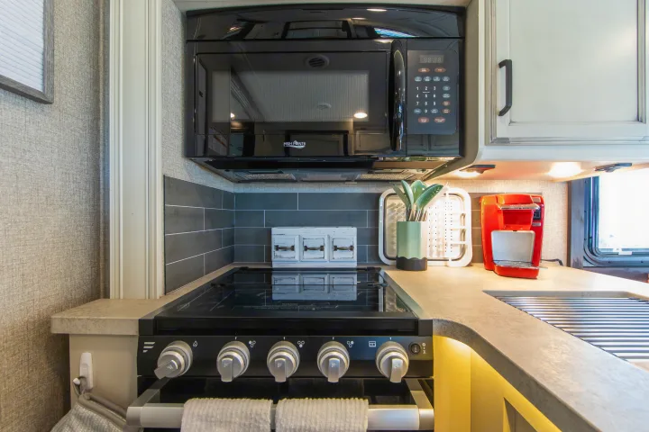 Compact RV rental kitchen featuring a microwave, stovetop, coffee maker, and sleek countertops.. Jayco Greyhawk 2021