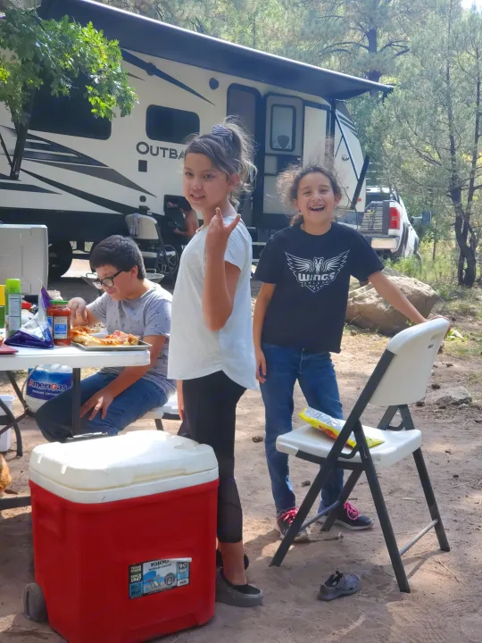 Family fun with an RV rental! Kids enjoy pizza outdoors by their travel trailer at a campsite.. Keystone Outback 2020