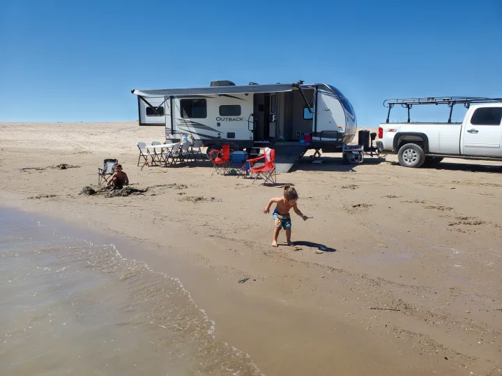 Beach day with an RV rental: Kids play by the water near an Outback travel trailer and truck.. Keystone Outback 2020