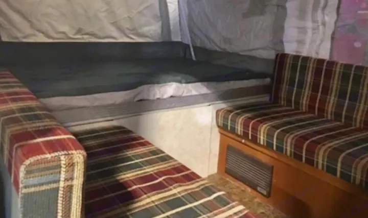 RV rental: Compact pop-up camper interior with a bed area and two plaid dinette benches. Ideal for camping.. Coleman Destiny Taos 1999