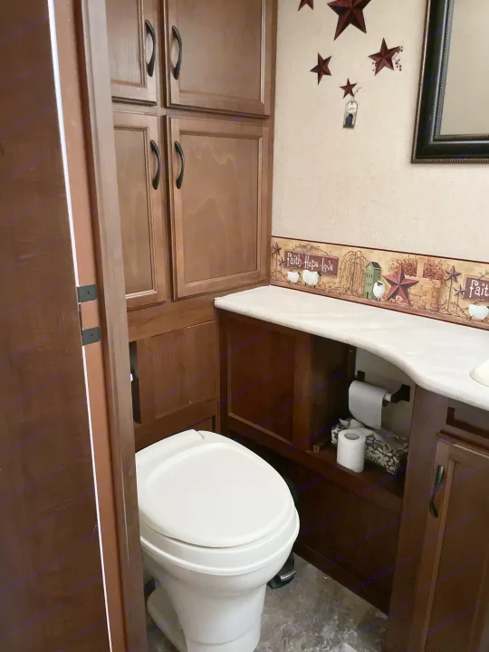 Compact RV rental bathroom features wood cabinets, a countertop, and a white toilet, providing functional and cozy space.. Jayco Jay Feather Ultra Lite 2015