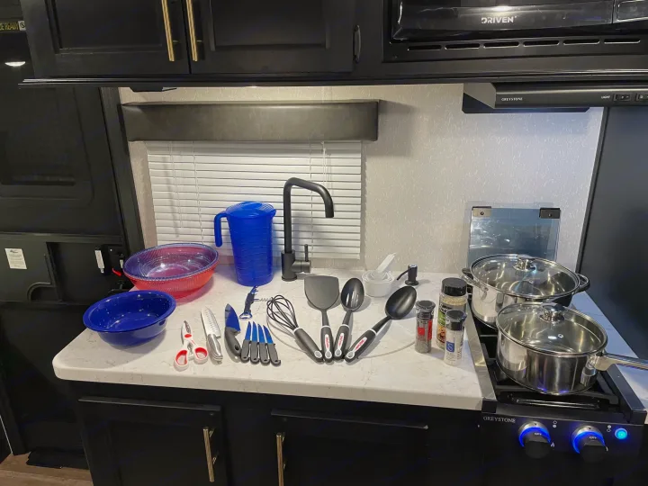 RV rental kitchen: fully equipped with cooking essentials, including pots, pans, utensils, spices, and bowls on the counter.. Forest River Wolf Den 16EV 2021
