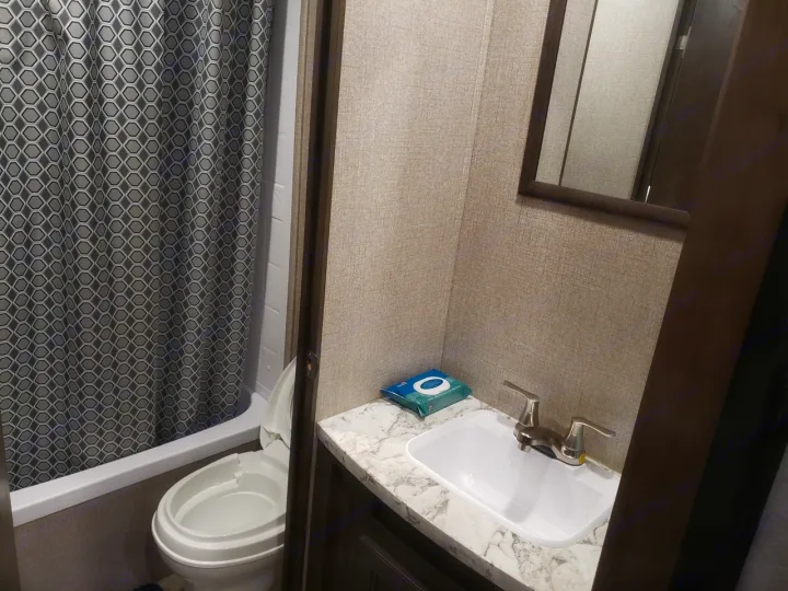 This RV rental bathroom features a compact toilet, shower with patterned curtain, and sink with counter. Ideal for camper travel.. Jayco Jay Flight SLX 2021