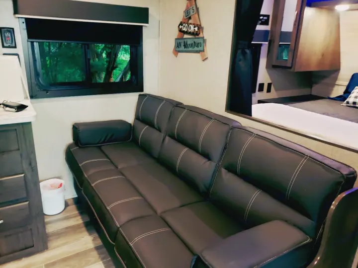 Step into an RV rental's inviting living space, featuring a dark sofa, window view of trees, and adjacent bedroom.. Jayco Jay Flight SLX 2021