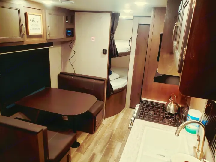 This cozy rv rental interior features a dining area, bunk beds, and a compact kitchen, perfect for travel comfort.. Jayco Jay Flight SLX 2021
