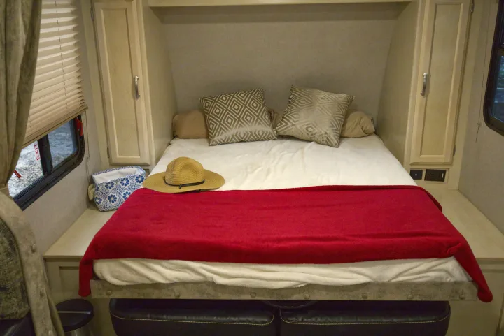 Comfortable RV rental bedroom setup with a bed, red blanket, decorative pillows, and essential power outlets.. Other Other 2019