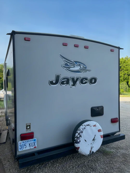 This Jayco travel trailer, an excellent RV rental option, is parked outdoors, featuring a Kansas plate and spare tire.. Jayco Jay Feather Ultra Lite 2015