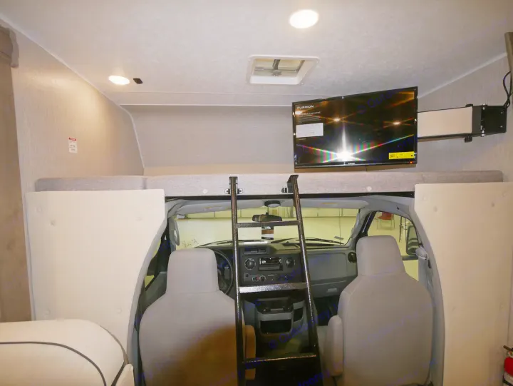 Inside an RV rental: view of the cockpit, over-cab bunk with ladder, and TV, offering a cozy travel living space.. Coachmen Freelander 23FS 2022