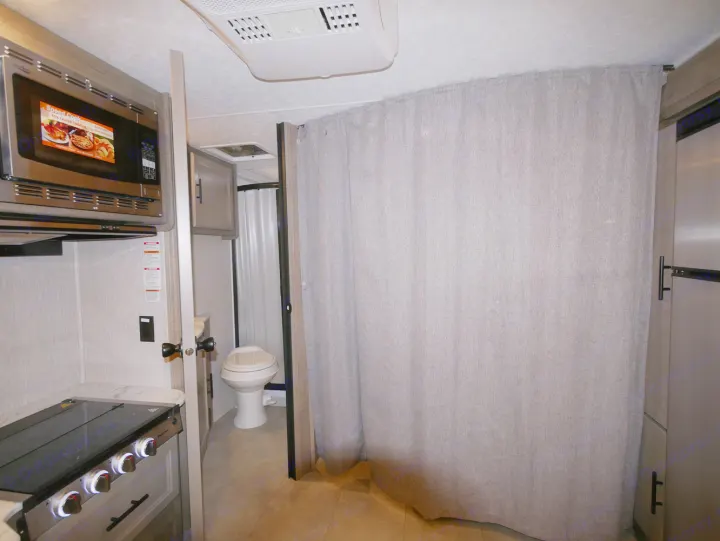 Inside this RV rental: full kitchen with microwave, private bathroom, and a large curtain separating living/sleeping space.. Coachmen Freelander 23FS 2022