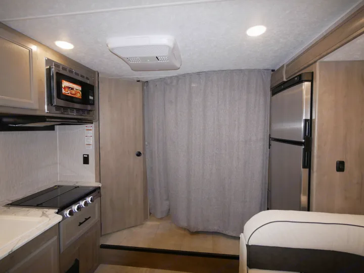 Modern RV rental interior with compact kitchen, microwave, fridge, and bed area. Great for your next adventure!. Coachmen Freelander 23FS 2022