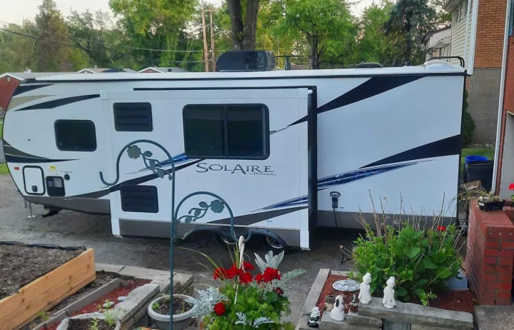 A white Palomino SolAire travel trailer, available for RV rental, parked in a residential yard. Note the extended slide-out.. Palomino Solaire 243bhs 2021
