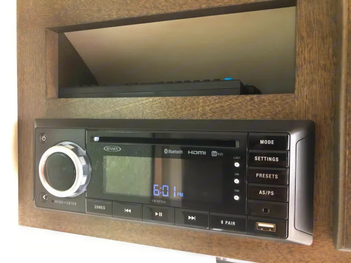 An RV rental's Jensen JWM70A stereo, displaying 6:01 PM, with a remote in a cubby above, is ready for entertainment.. T@B T@B 320 OffRoad 2020