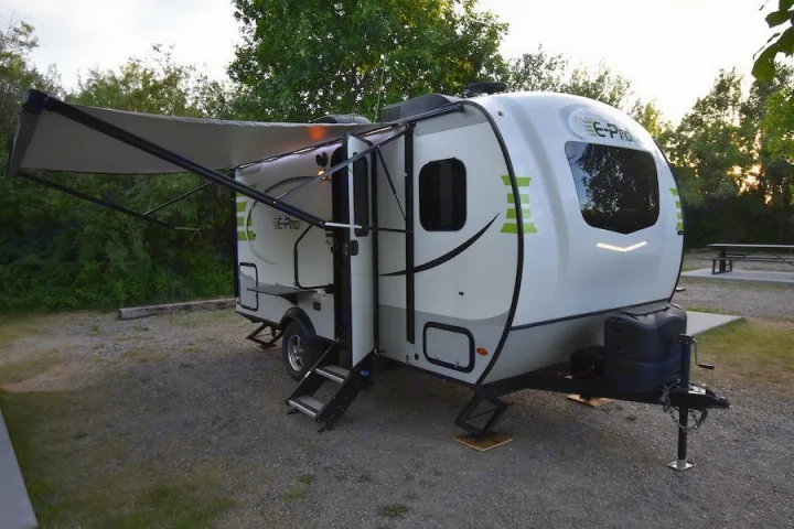 This white and lime green E-Pro RV rental is parked with its awning extended at a gravel campsite, perfect for outdoor trips.. Forest River Flagstaff E-Pro 2019