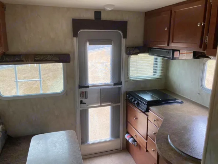 Clean RV rental interior featuring a compact kitchen with stove, cabinets, dining table, and windows. Ready for adventure!. Northwood Mfg Wolf Creek 2017