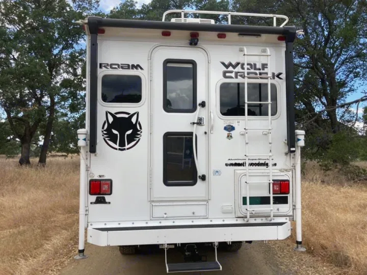Rear of a white Wolf Creek truck camper, 'ROAM' branded with a wolf decal, parked outdoors. Explore this RV rental.. Northwood Mfg Wolf Creek 2017