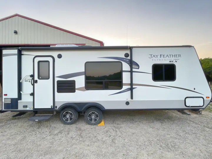 This white Jayco Jay Feather travel trailer, ideal for an RV rental adventure, is parked on a gravel lot.. Jayco Jay Feather Ultra Lite 2015