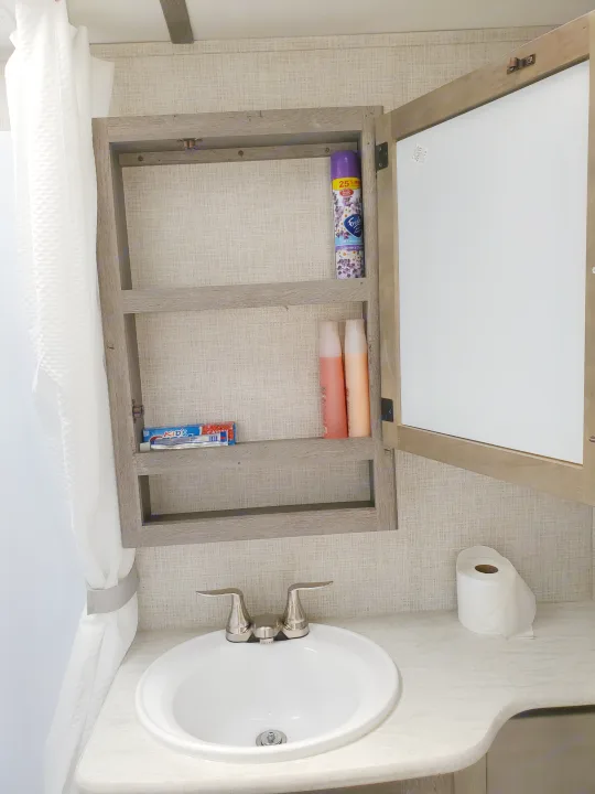 Compact RV rental bathroom featuring a sink, toilet paper, and an open medicine cabinet stocked with toiletries.. Keystone Outback 2020