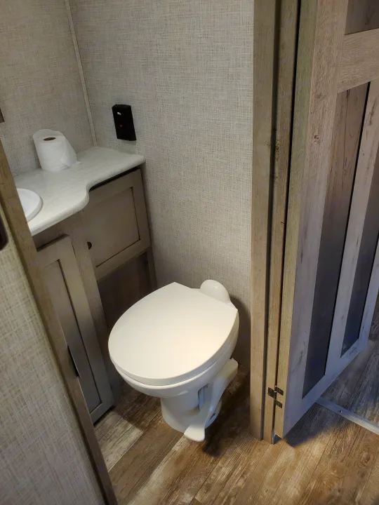 Compact RV rental bathroom featuring a toilet, vanity, and wood-look floor, ready for your travels.. Keystone Outback 2020