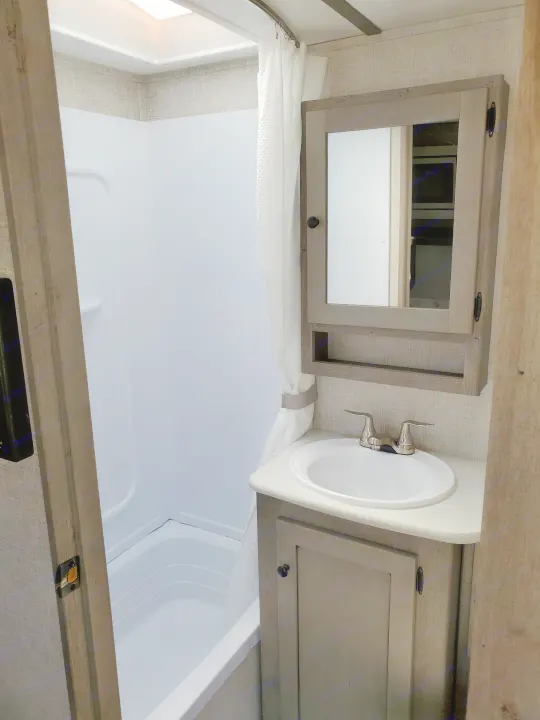 Clean, modern RV rental bathroom featuring a tub/shower combo, vanity with sink, and mirrored medicine cabinet.. Keystone Outback 2020