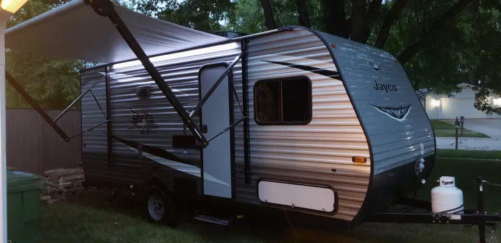 A gray Jayco travel trailer with a bright awning extended is set up, ideal for your next RV rental.. Jayco Jay Flight 2021