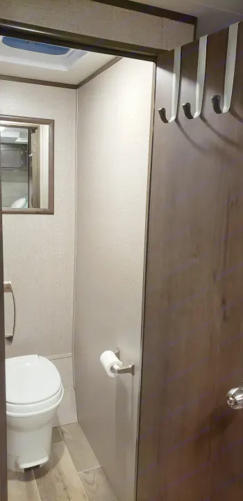 Inside an RV rental bathroom featuring a toilet, mirror, overhead vent, and practical door hooks. Compact and functional.. Jayco Jay Flight 2021