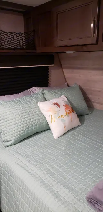 Cozy RV rental bedroom with light green quilted bedding, 'Wander' pillow, and overhead storage. Perfect for your next trip.. Jayco Jay Flight 2021