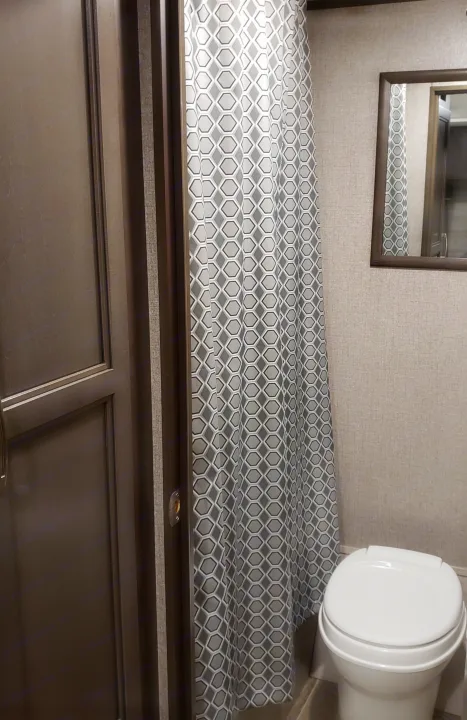 Compact RV rental bathroom with a gray hexagonal shower curtain, white toilet, and dark-framed wall mirror.. Jayco Jay Flight 2021