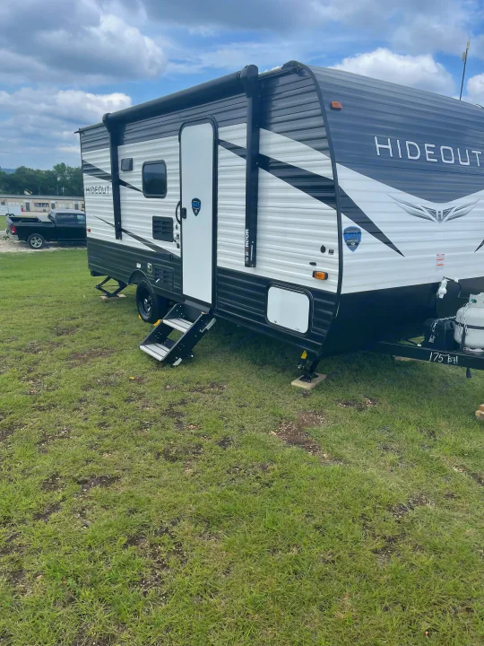 A black and white Hideout travel trailer is parked on grass with steps extended. Great for an rv rental.. keystone Hideout 2021