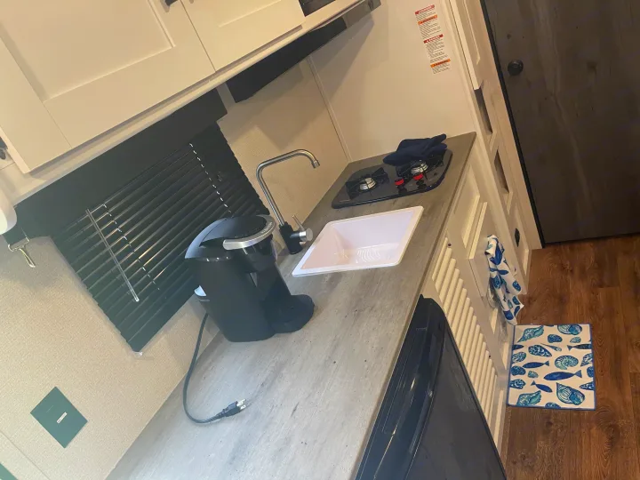 An RV rental's practical kitchen area with a counter, sink, Keurig, and stove, ideal for travel adventures.. keystone Hideout 2021
