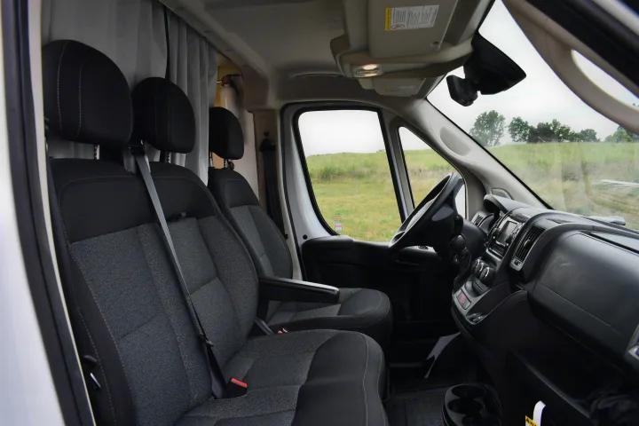 RV rental van's front cabin: driver & passenger seats, dashboard, and a clear view of a grassy field outside.. Other Other 2021