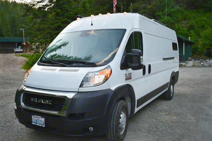 A bright white Ram ProMaster camper van, an rv rental, with orange marker lights, parked on gravel.. Other Other 2021