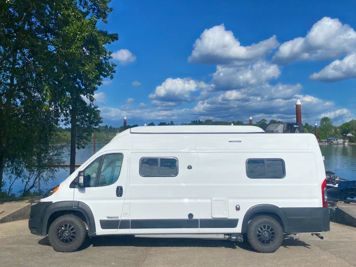 White RV rental camper van with all-terrain tires parked on a sunny day by the water.. Winnebago Winnebago 2021