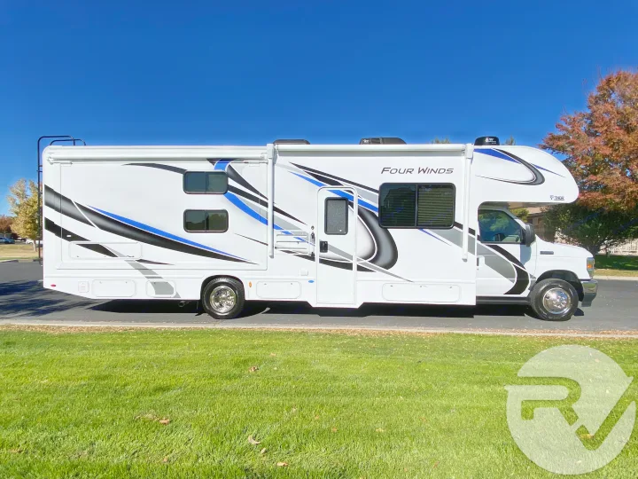 White Thor Four Winds motorhome RV rental with blue & black graphics, parked on pavement by grass under a clear sky.. Thor Motor Coach Four Winds 2021