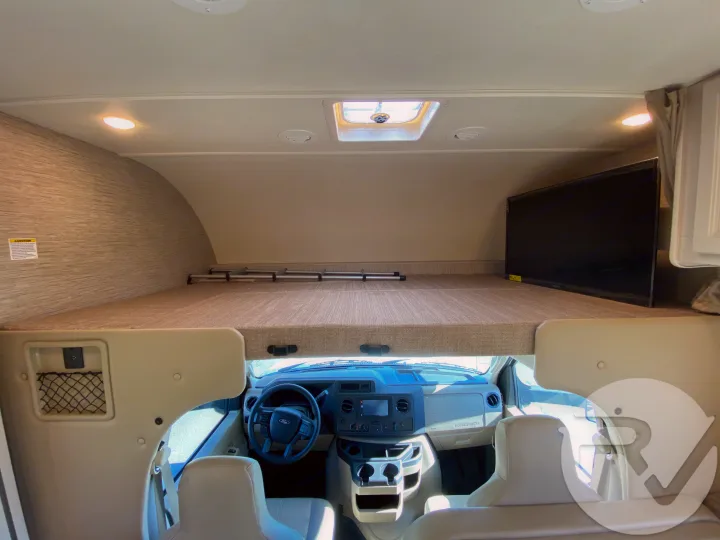 Spacious RV rental interior: cab-over bunk bed with TV, plus the Ford E-series dashboard and seats.. Thor Motor Coach Four Winds 2021