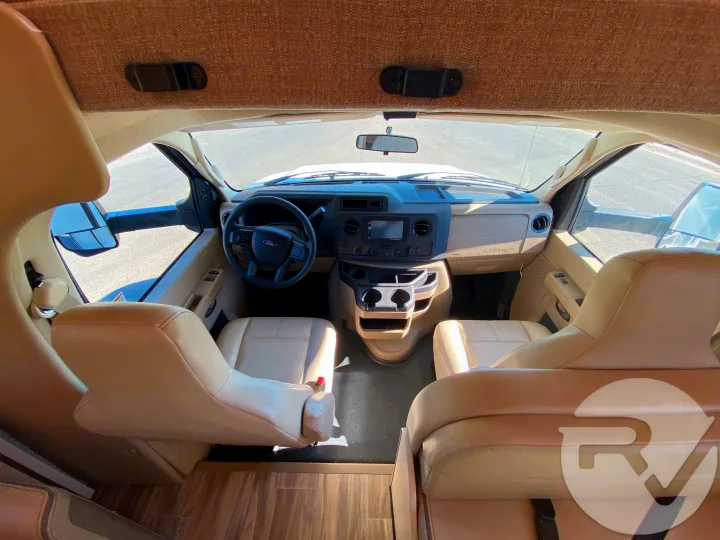 Explore the interior of an RV rental: A wide view of the spacious cockpit with beige seats, steering wheel, and dashboard.. Thor Motor Coach Four Winds 2021