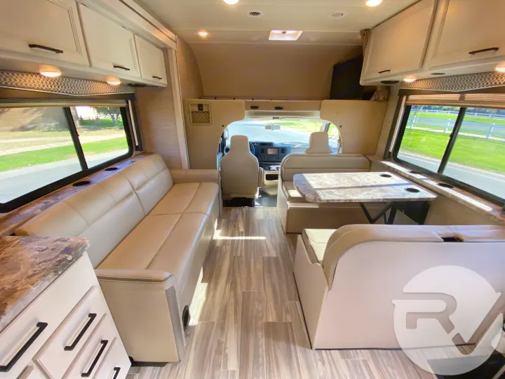 Bright and spacious RV rental interior features lounge seating, dining booth, and driver's cab. Perfect for trips.. Thor Motor Coach Four Winds 2021