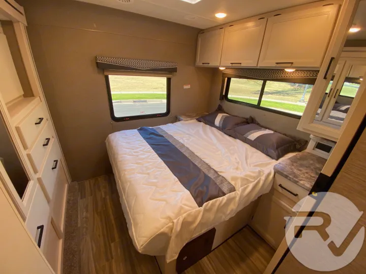 Cozy RV rental bedroom featuring a queen bed with gray bedding, overhead cabinets, and built-in storage.. Thor Motor Coach Four Winds 2021