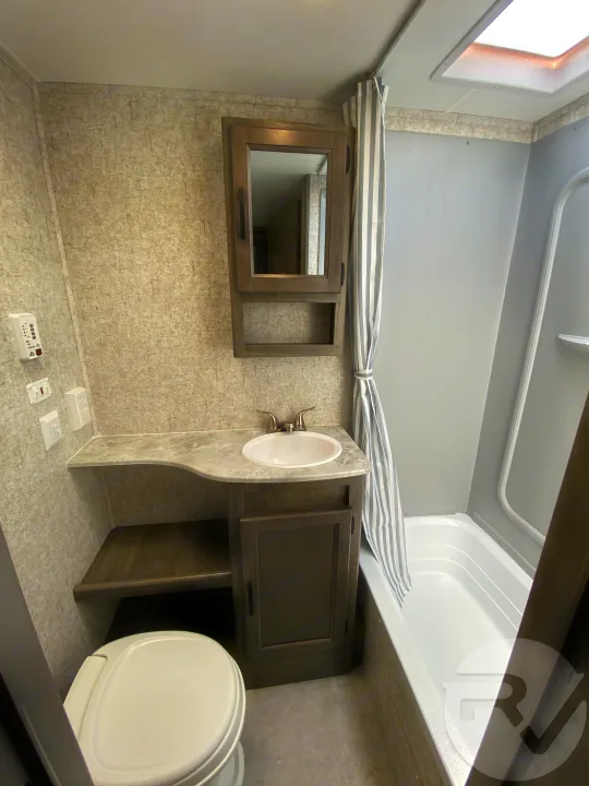 This RV rental bathroom features a toilet, sink vanity, mirrored cabinet, and shower/tub with skylight. Clean & functional.. Coachmen Apex 2021