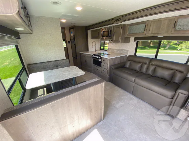 Inside a stylish RV rental: full kitchen, dinette, and sofa. Enjoy the road trip in comfort with this modern living space.. Coachmen Apex 2021