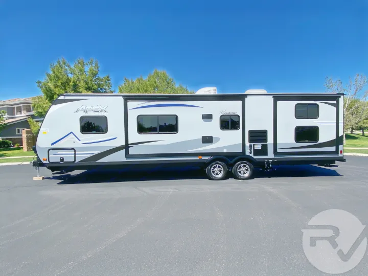 Light gray Coachmen Apex travel trailer, a two-axle RV ready for rv rental, parked on asphalt under a blue sky.. Coachmen Apex 2021