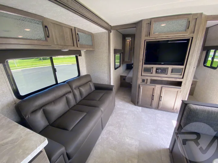 Inside this **rv rental**: A well-appointed living space with a large sofa, entertainment system, and access to a sleeping area.. Coachmen Apex 2021