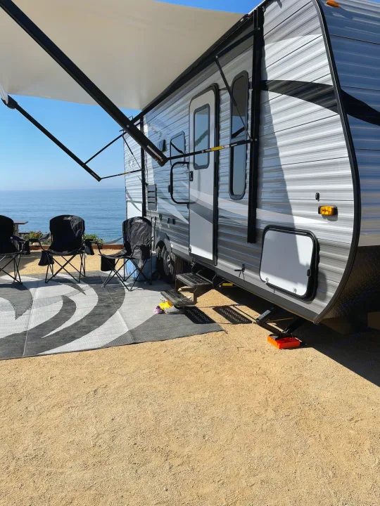 Oceanfront RV rental, featuring an extended awning, outdoor chairs, and a mat on the gravel campsite.. Jayco Jayflight 224bhw 2021