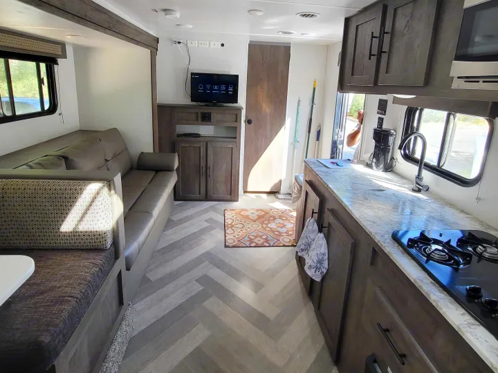 Inside a modern RV rental: living area with sofa, kitchen with stove and sink, and light wood herringbone floor.. Forest River EVO 2020
