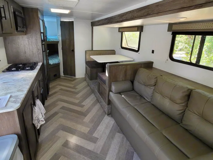 Bright rv rental showing a functional kitchen, dining area, lounge sofa, and private bunk beds.. Forest River EVO 2020