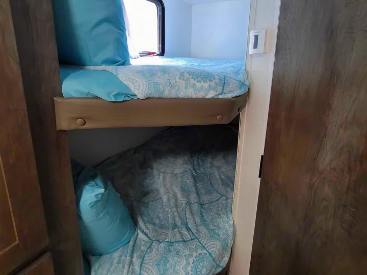 RV rental bunk beds with light blue bedding, providing a cozy sleeping area in a compact camper interior.. Forest River EVO 2020