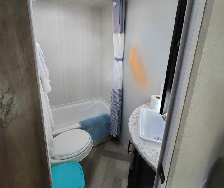 Compact RV rental bathroom with white toilet, tub/shower with striped curtain, and a sink on a marbled counter.. Forest River EVO 2020