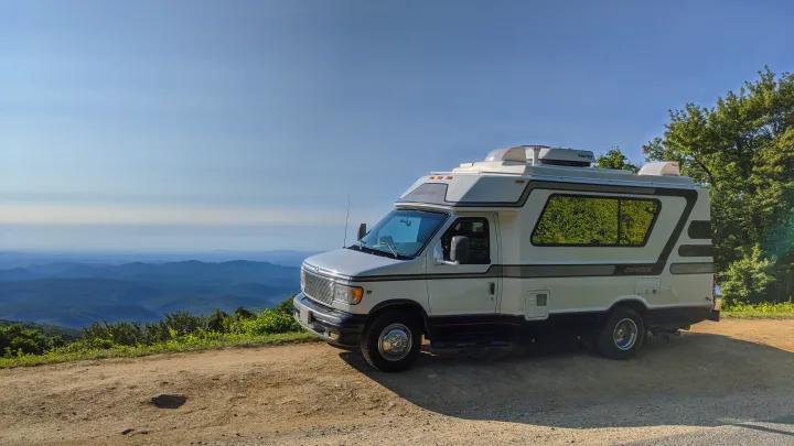 White RV rental on a dirt road overlook, offering panoramic blue mountain views under a clear sky. Ready for your next adventure.. Chinook Concourse 2001