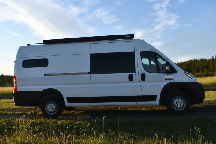 White Ram ProMaster camper van conversion, ideal for your next RV rental. Parked outdoors with an awning visible on the roof.. Other Other 2021